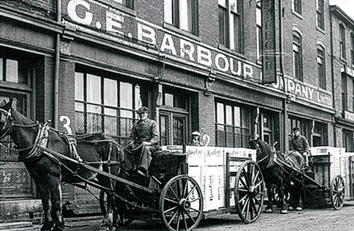 Black and white historical photograph showing horse-drawn carts on a city street in front of a building with large signage reading G.E. Barbours.